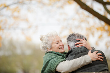 Smiling, affectionate senior couple hugging on bench in autumn park