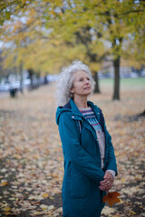 Senior woman standing amoung leaves in autumn park