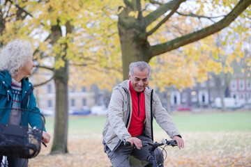 Senior couple bike riding among trees and leaves in autumn park