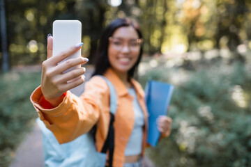 blurred asian woman taking selfie on mobile phone in park