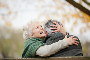 Smiling, affectionate senior couple hugging on bench in autumn park