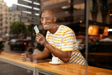 Handsome young african man in cafe drinking coffee. Portrait of happy man with credit card drinking coffee in cafe.
