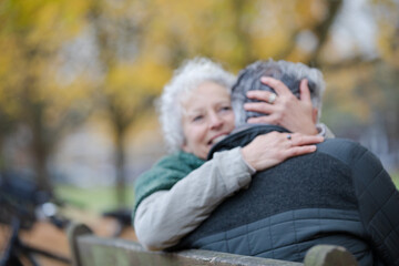 Fototapeta premium Smiling, affectionate senior couple hugging on bench in autumn park