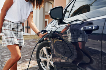 Naklejka premium Process of charging the vehicle by electricity. Woman is outdoors with her modern automobile