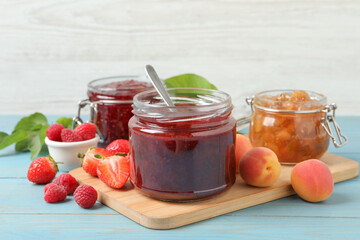 Jars with different jams and fresh fruits on light blue wooden table