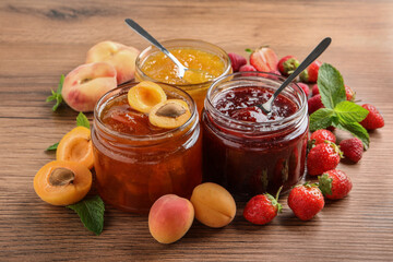 Jars with different jams and fresh fruits on wooden table