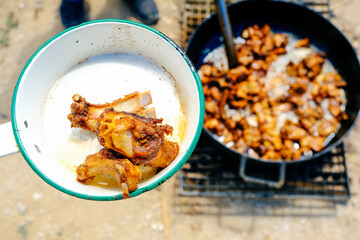 Fresh fried pork served in white saucepan while meat frying in cooking pot at farm