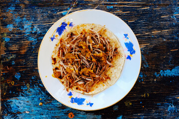 Cooked shredded meat on fresh tortilla served in plate kept on wooden table