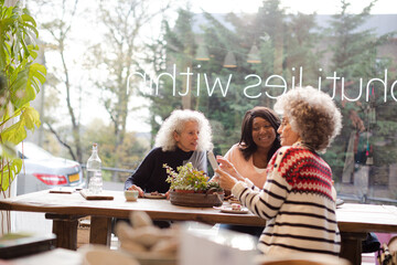 Senior women friends using smart phone, drinking coffee at autumn park cafe
