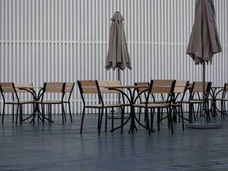 An open-air cafe is preparing to receive guests. New furniture for the cafe is installed. Tables and chairs made of black metal and light wood on a dark gray floor.