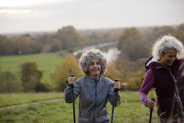 Active senior women friends with walking sticks in autumn park