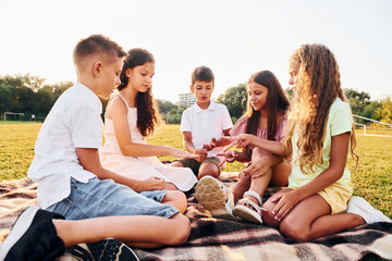 Fototapeta premium Communicating with each other. Group of happy kids is outdoors on the sportive field at daytime
