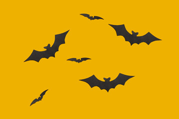 Halloween flat lay composition of black paper bats fly up on orange background, top view.