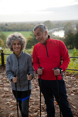 Smiling, affectionate senior couple with walking sticks in park