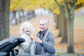Affectionate, tender senior couple hugging in autumn park near car