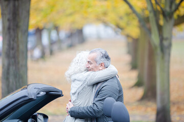Fototapeta premium Affectionate, tender senior couple hugging in autumn park near car