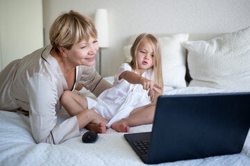 little girl with her grandmother sitting on the bed in front of a laptop