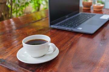 Coffee cup and laptop on a wooden table in the garden