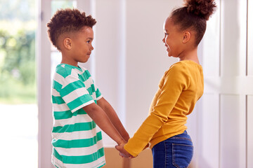 Brother And Sister Holding Hands Standing In Hallway Of New Home