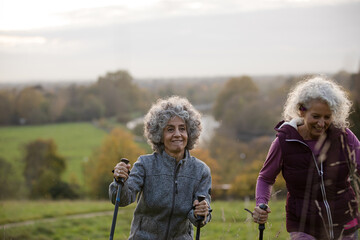 Active senior women friends with walking sticks in autumn park