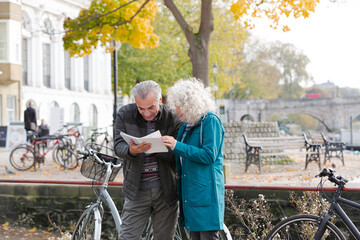 Senior couple with bicycles traveling, looking at guidebook along autumn river