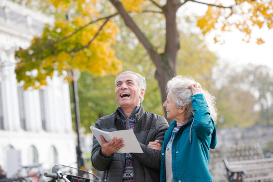 Senior couple with bicycles traveling, looking at guidebook along autumn river - Powered by Adobe