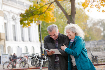Senior couple with bicycles traveling, looking at guidebook along autumn river