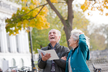 Senior couple with bicycles traveling, looking at guidebook along autumn river