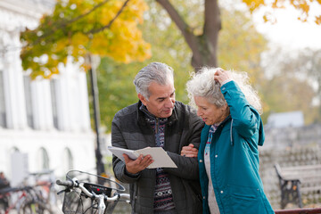 Senior couple with bicycles traveling, looking at guidebook along autumn river