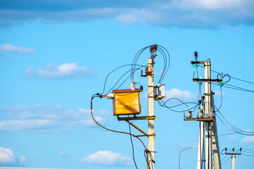 Electric poles with wires and a junction box against a blue sky with clouds.
