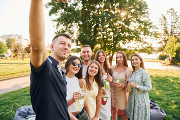 Man taking a selfie. Group of young people have a party in the park at summer daytime