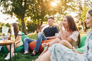 Sitting in the armchair bags and smoking hookah. Group of young people have a party in the park at summer daytime