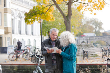 Senior couple with bicycles traveling, looking at guidebook along autumn river