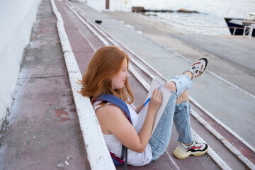 teenage girl draws in the sketchbook while sitting on the steps