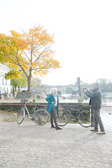 Obraz premium Senior man photographing wife with bicycle in autumn city
