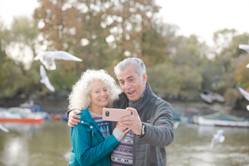 Playful senior couple taking selfie at pond in park