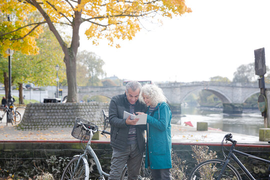 Senior couple with bicycles traveling, looking at guidebook along autumn river - Powered by Adobe