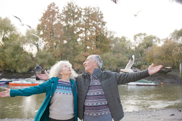 Smiling, affectionate senior couple hugging in park with flying birds