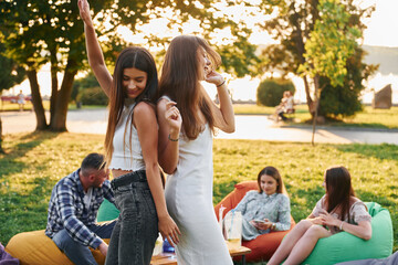 Women posing for the camera. Group of young people have a party in the park at summer daytime