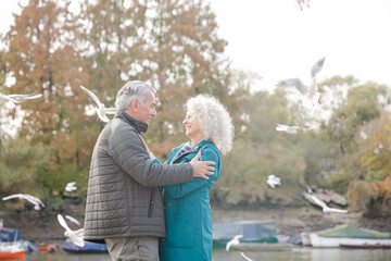 Affectionate active senior couple hugging at park pond