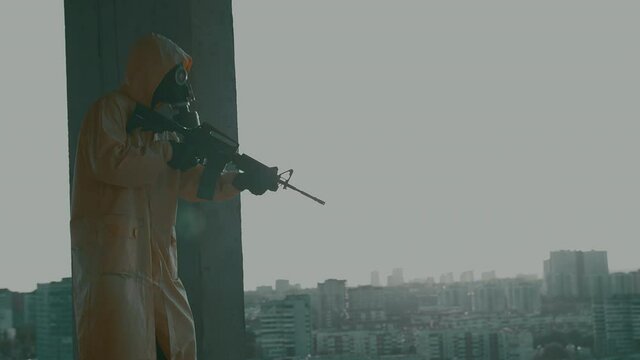 man in gas mask, protective suit, with weapon stands on the edge of high-rise unfinished building and sharply aims. Atmosphere of the post-apocalypse, the consequences of man-made disaster, pandemic.