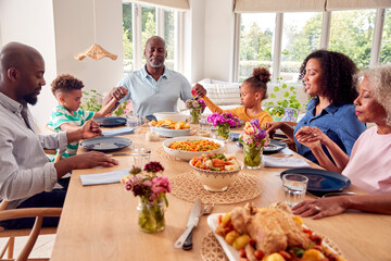 Multi Generation Family Holding Hands Around Table At Home Saying Grace Before Eating Meal Together