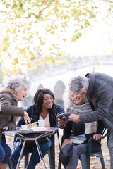 Active senior friends using digital camera at autumn sidewalk cafe
