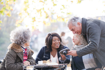Fototapeta na wymiar Active senior friends using digital camera at autumn sidewalk cafe