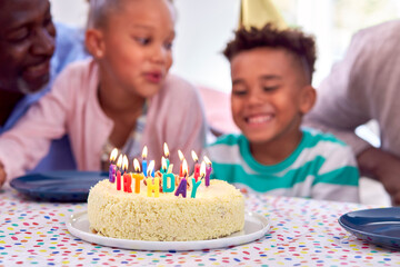 Family Sitting Around Table At Home Celebrating Boy's Birthday With Cake And Party