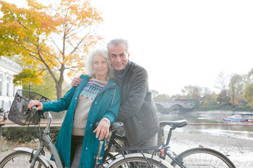 Portrait smiling senior couple bike riding along autumn river