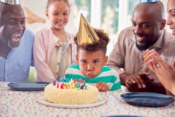 Multi Generation Family Sitting Around Table At Home Celebrating Boy's Birthday With Cake And Party