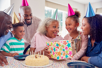 Multi Generation Family Around Table At Home Celebrating Grandmother's Birthday With Cake And Party