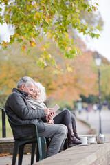 Active senior couple talking, enjoying coffee at autumn park cafe