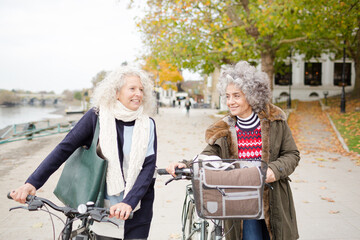Smiling active senior women walking bicycles in autumn park
